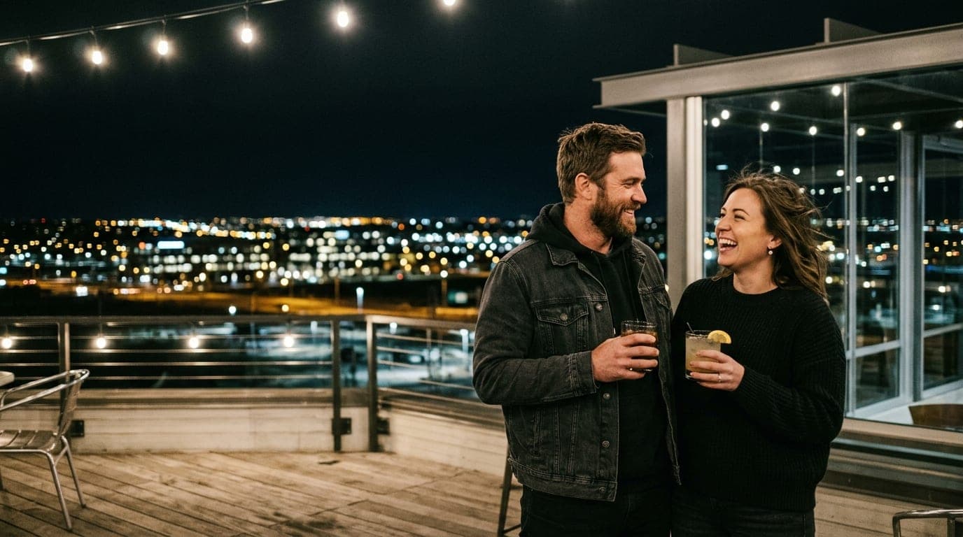 Low-angle 35mm documentary shot of a couple standing on the Pindustry rooftop in Centennial at midnight. They hold craft c...