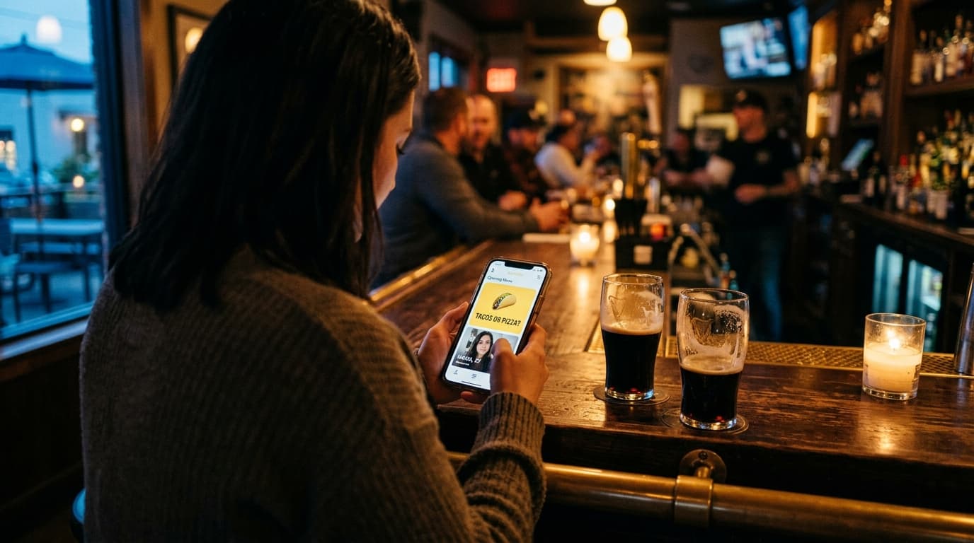 Over-the-shoulder view at a low-lit Stone Brewing bar. Selective focus draws the eye to a smartphone screen displaying a B...
