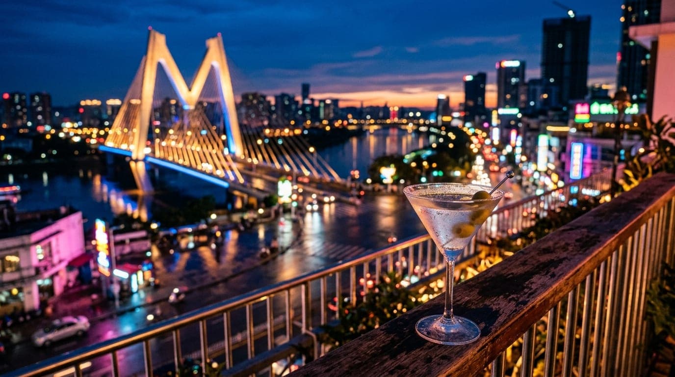 A close-up shot captures a chilled martini glass on a balcony railing in the lower third, with the illuminated M Bridge re...