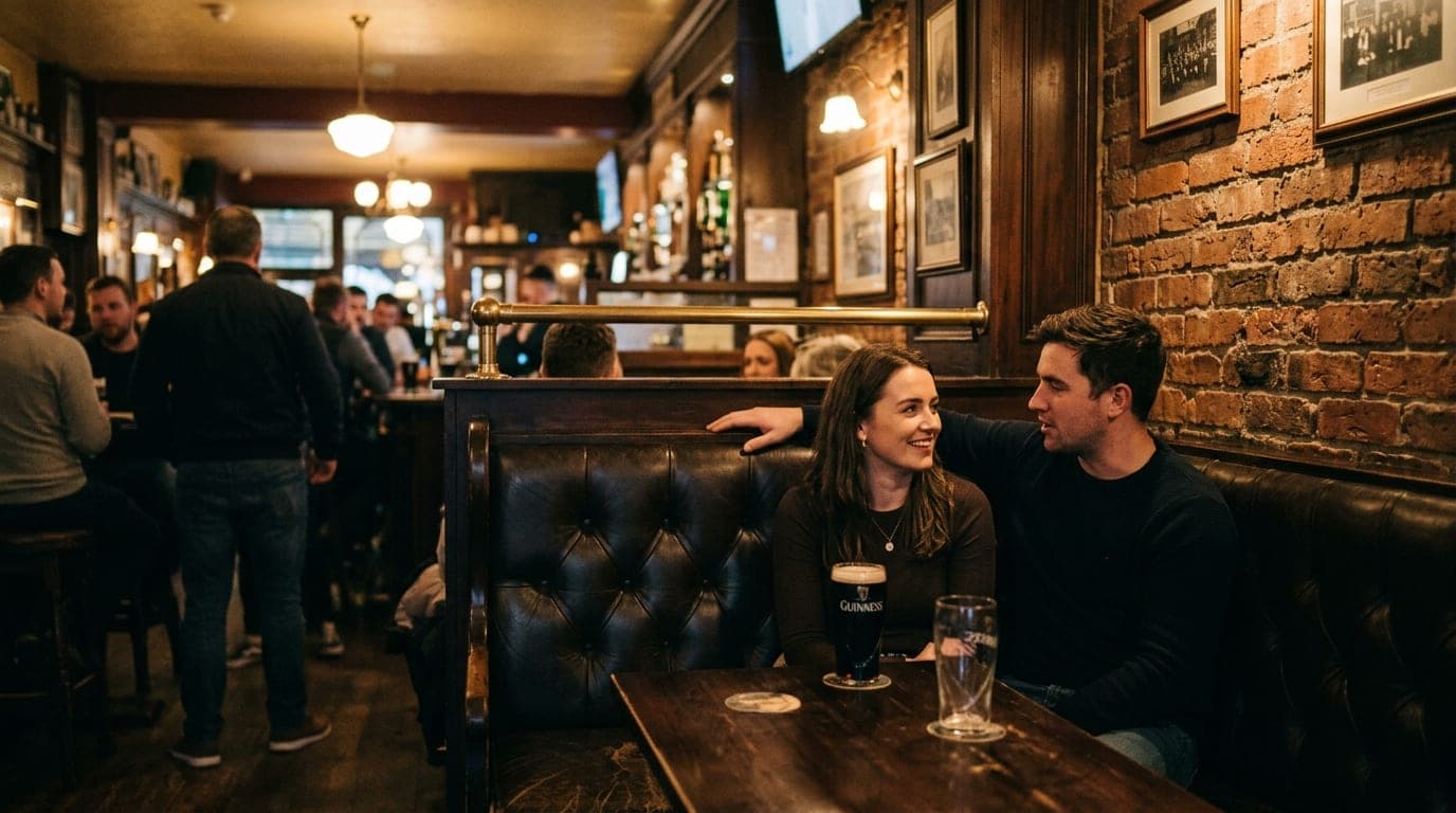 A wide, 35mm documentary shot of a couple sitting in a dark, high-backed leather booth at Dublin’s Irish Pub. Warm tungste...