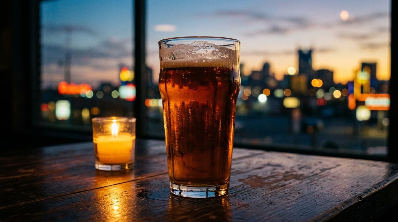 A 100mm macro shot of a single amber craft beer pint glass on a dark wood table, illuminated by flickering candlelight, re...