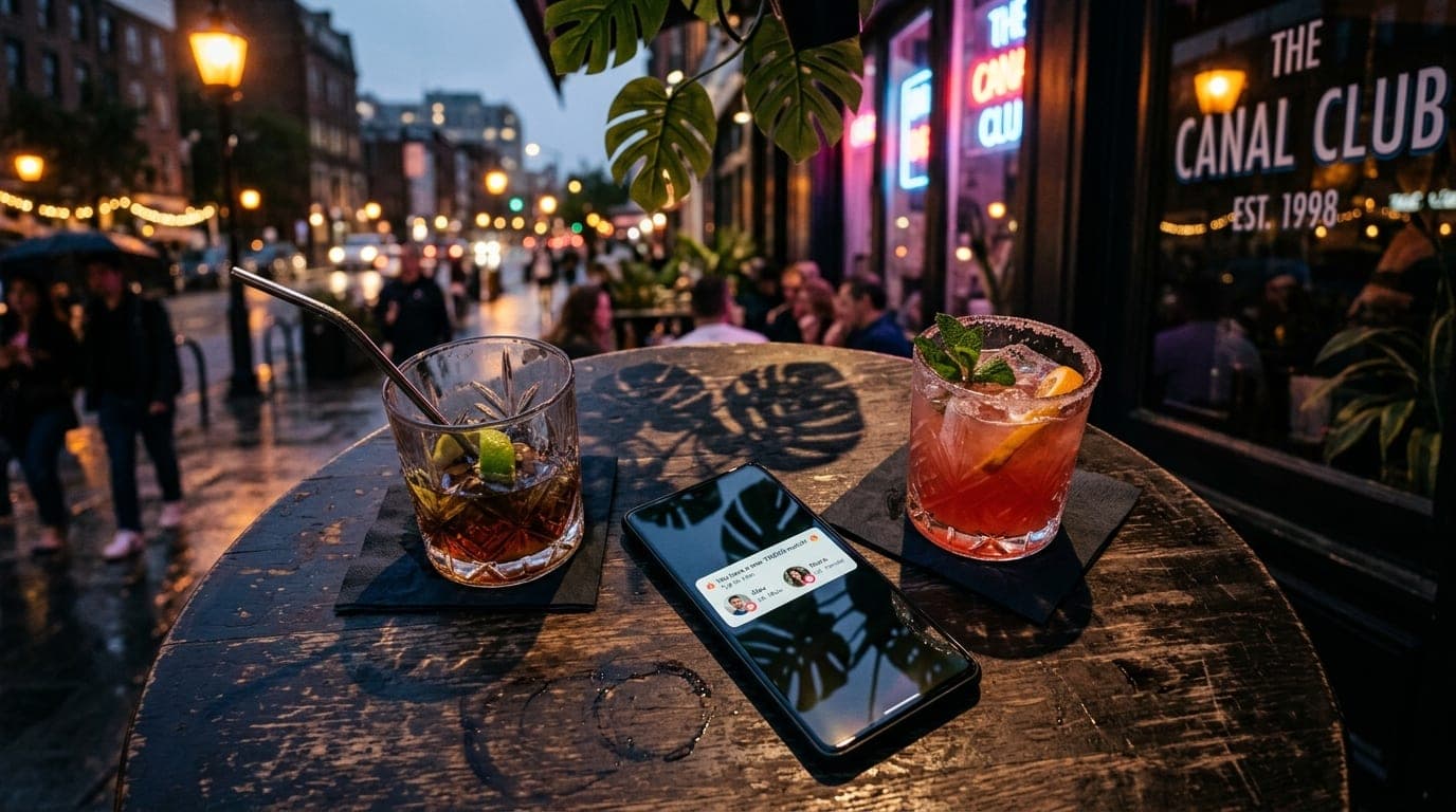 Overhead flat-lay of two half-empty cocktail glasses on a dark bistro table at The Canal Club. Tropical monstera shadows f...
