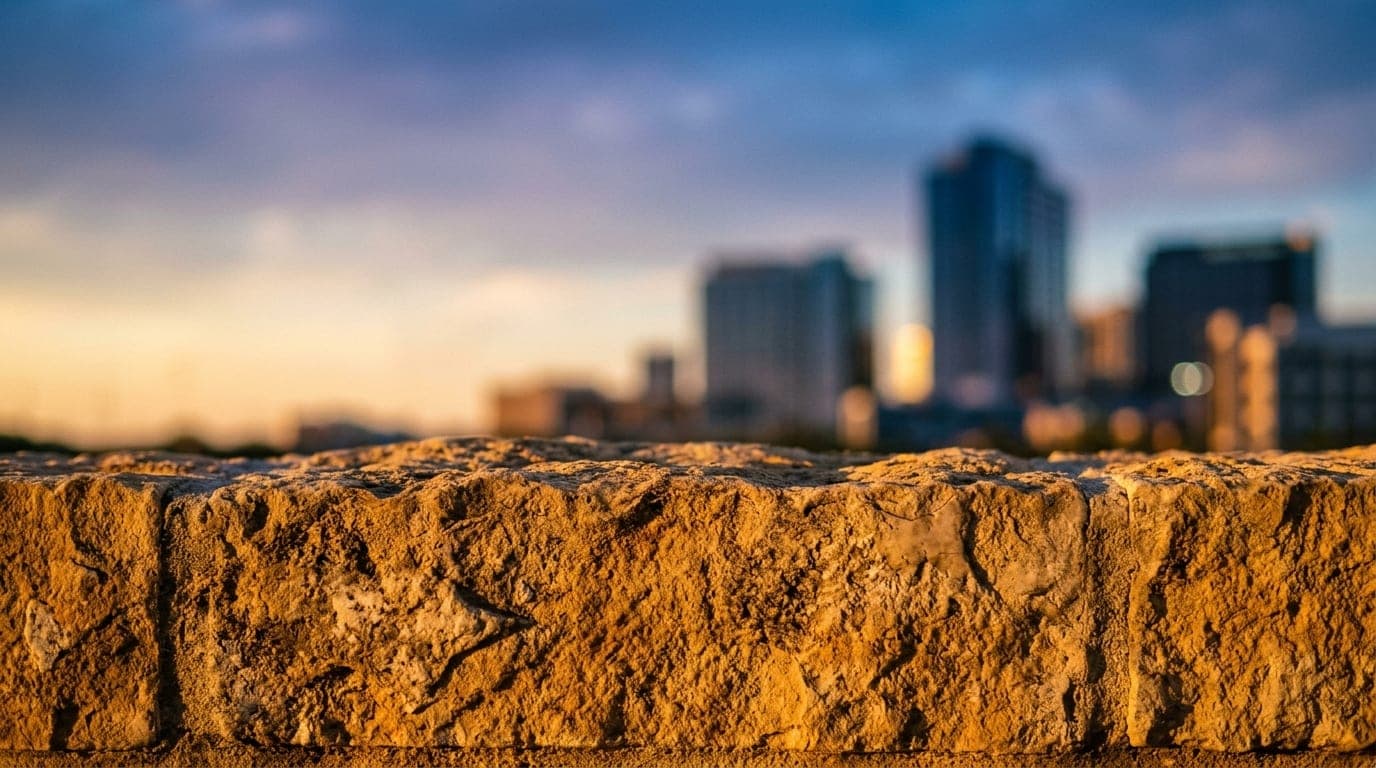 A macro, extreme close-up of amber golden hour sunlight reflecting off the textured limestone facade of a Legacy West high...