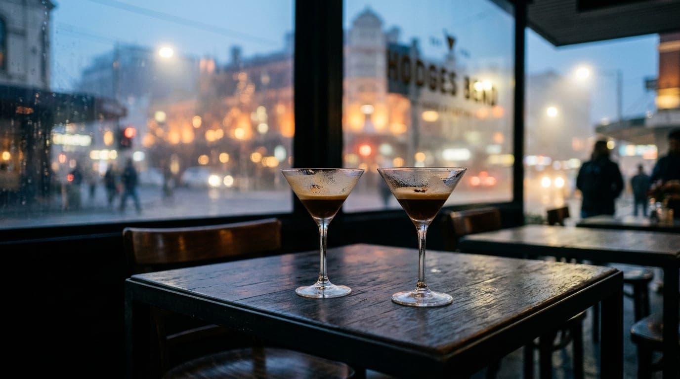 A low-angle hero shot captures two half-finished espresso martinis on a dark bistro table at Hodges Bend, with blurred, wa...