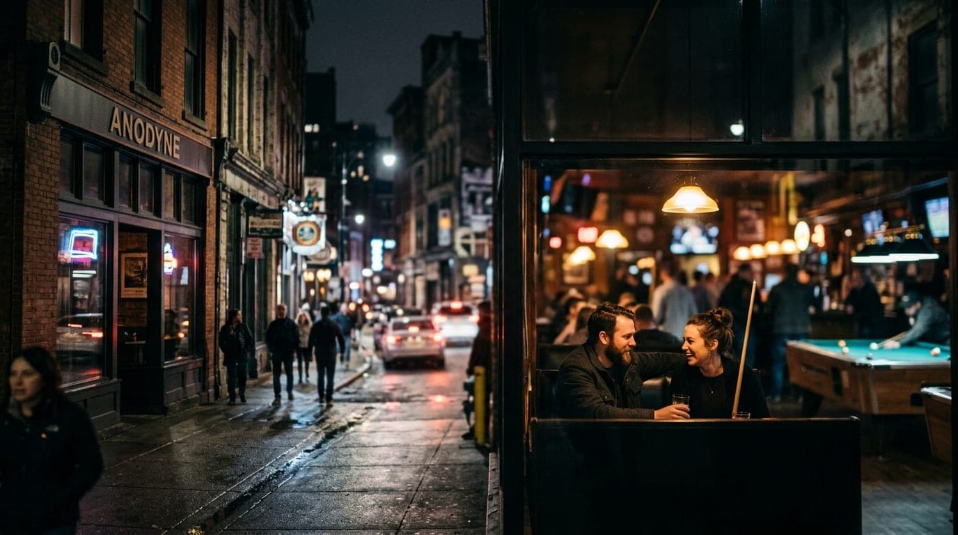 A wide establishing shot of the Anodyne pool hall at night. Selective focus highlights a couple in a dark booth, illuminat...