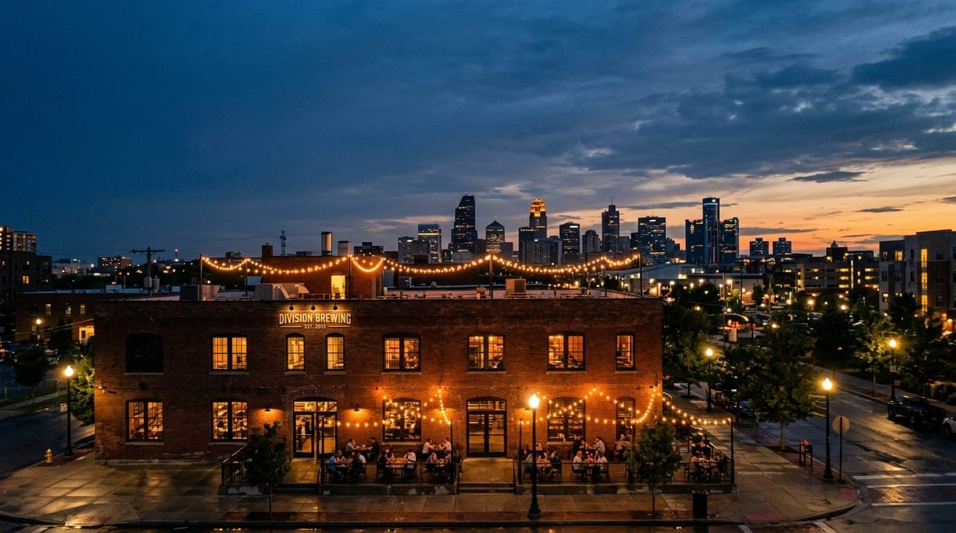 A wide shot of the Division Brewing brick facade at twilight, featuring glowing tungsten string lights hanging above the p...