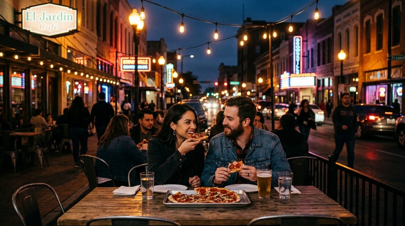A centered wide-angle shot of a couple sharing a thin-crust pizza at an outdoor cafe table in downtown Brownsville, illumi...