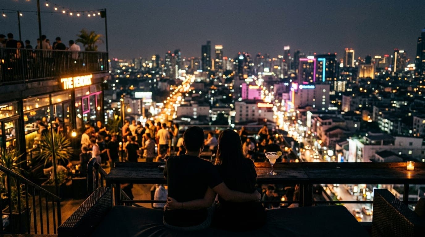 Wide establishing shot of The Hendrix rooftop at night. A couple sits in the lower third, silhouetted against glowing city...