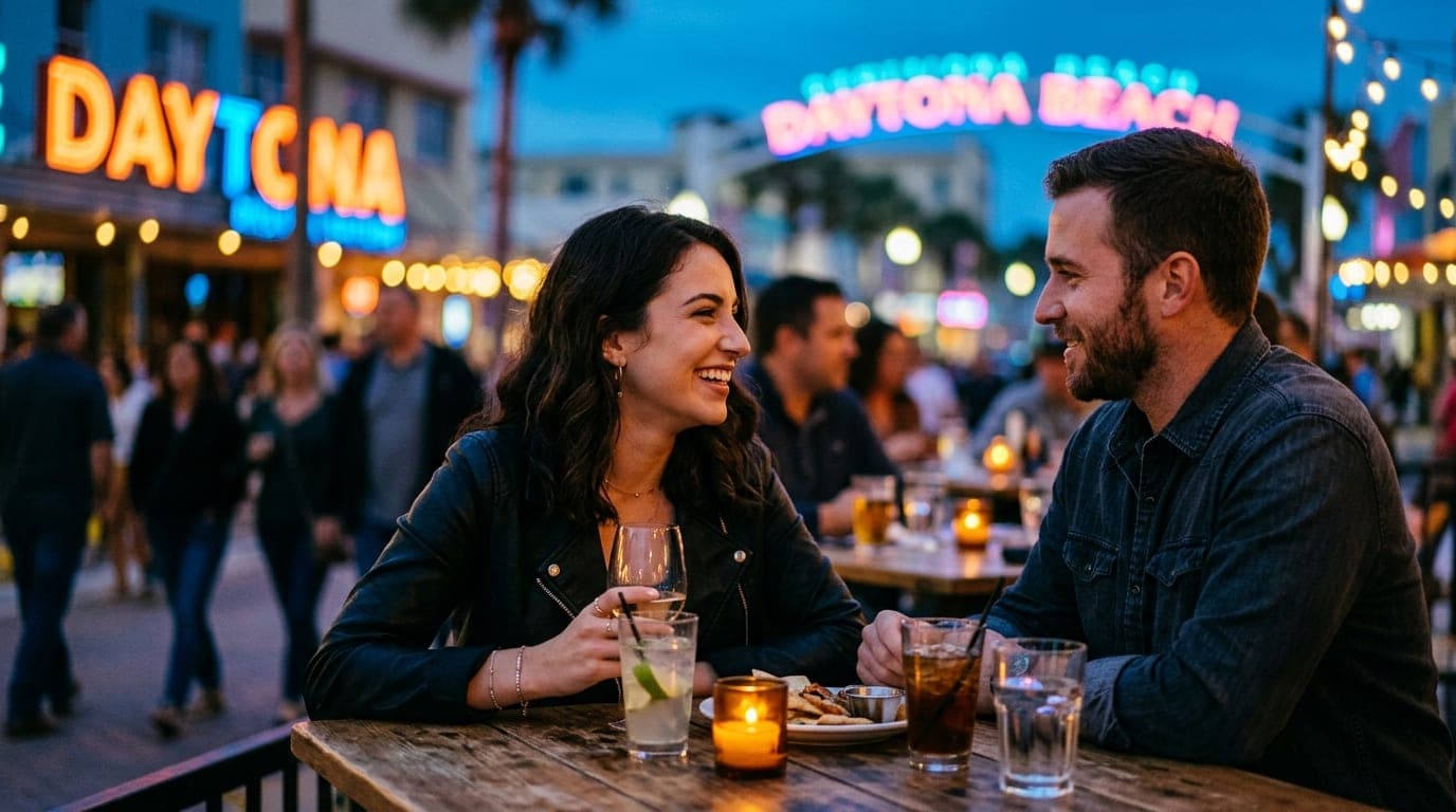 A couple sits at a crowded outdoor table at One Daytona, illuminated by soft blue hour ambient lighting. A blurred, vibran...