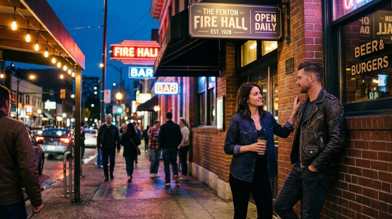 A 35mm documentary shot, rule-of-thirds with subjects offset right. A couple stands outside The Fenton Fire Hall at night;...