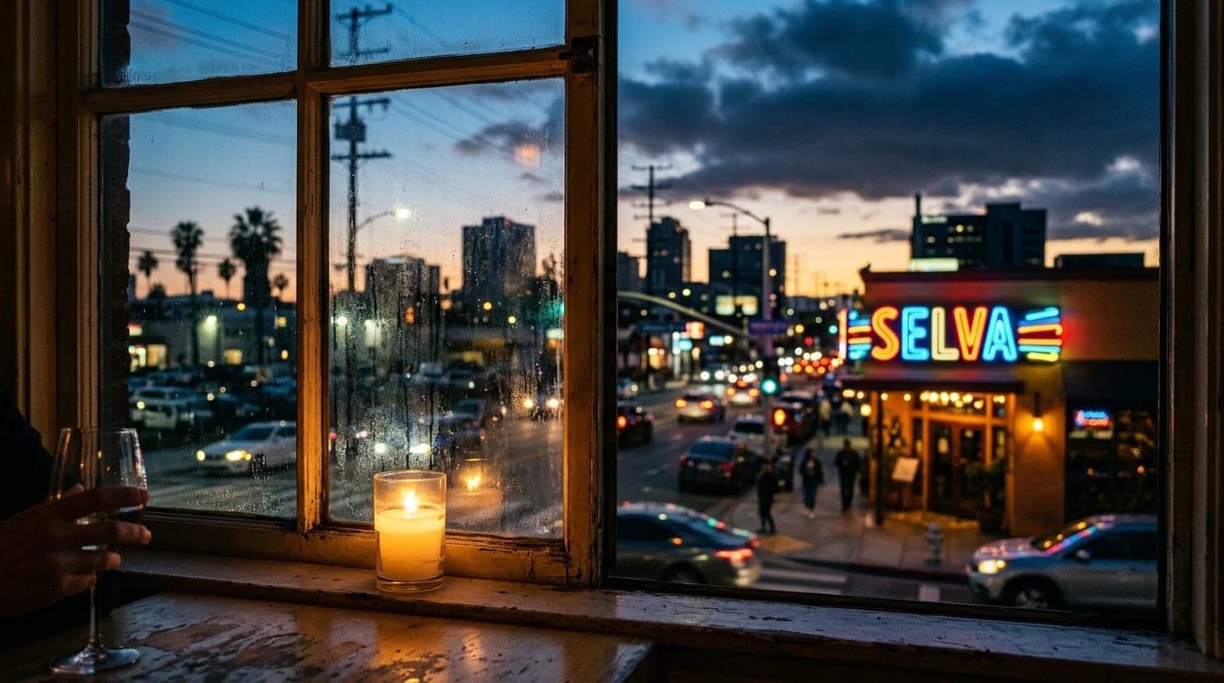 A medium 35mm shot through a candle-lit windowpane on Anaheim Street. The vibrant, blurred neon glow of the Selva exterior...
