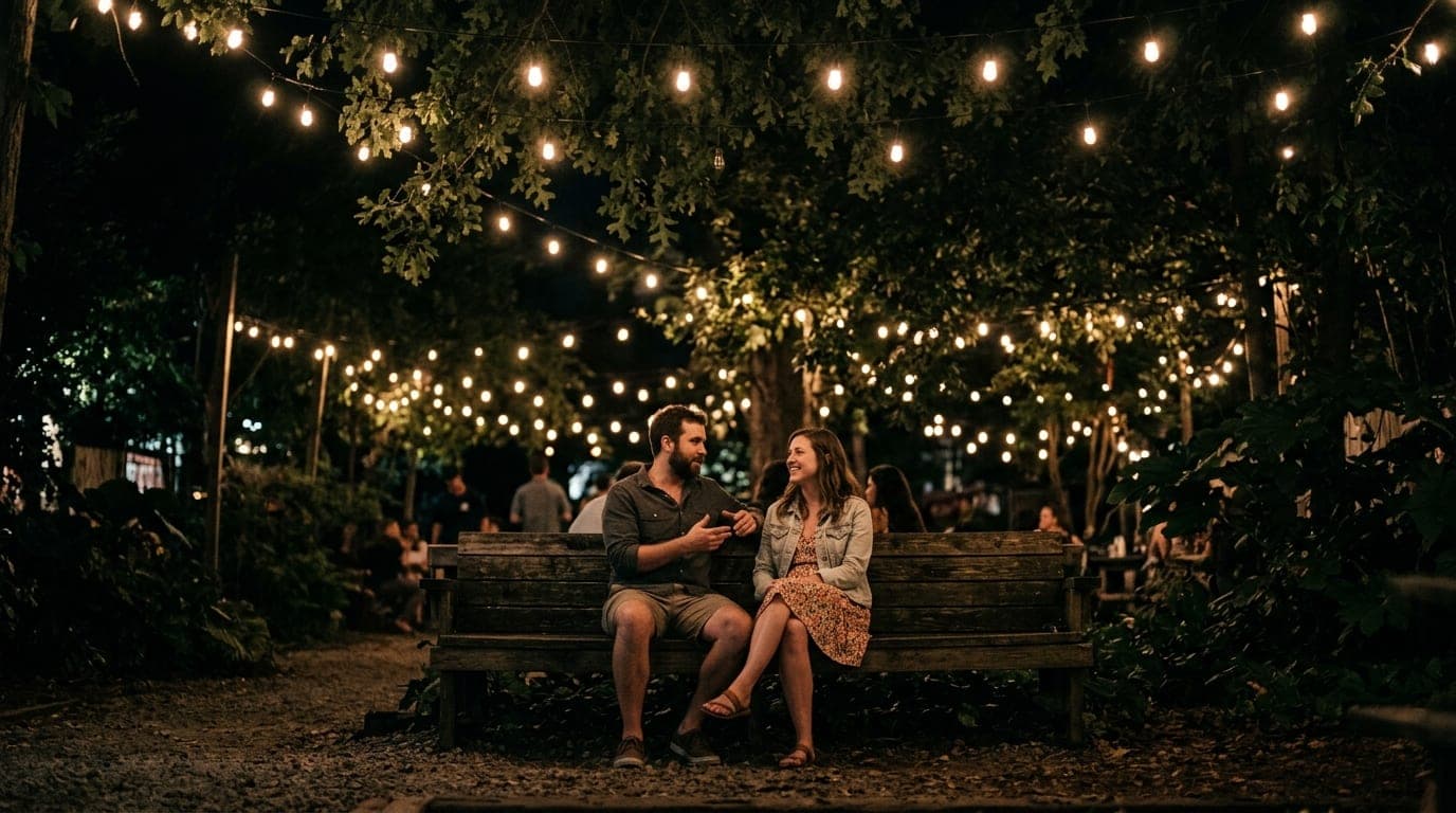 Low-angle hero shot at midnight inside Society Garden. A couple in casual summer attire sits on a weathered wooden bench,...