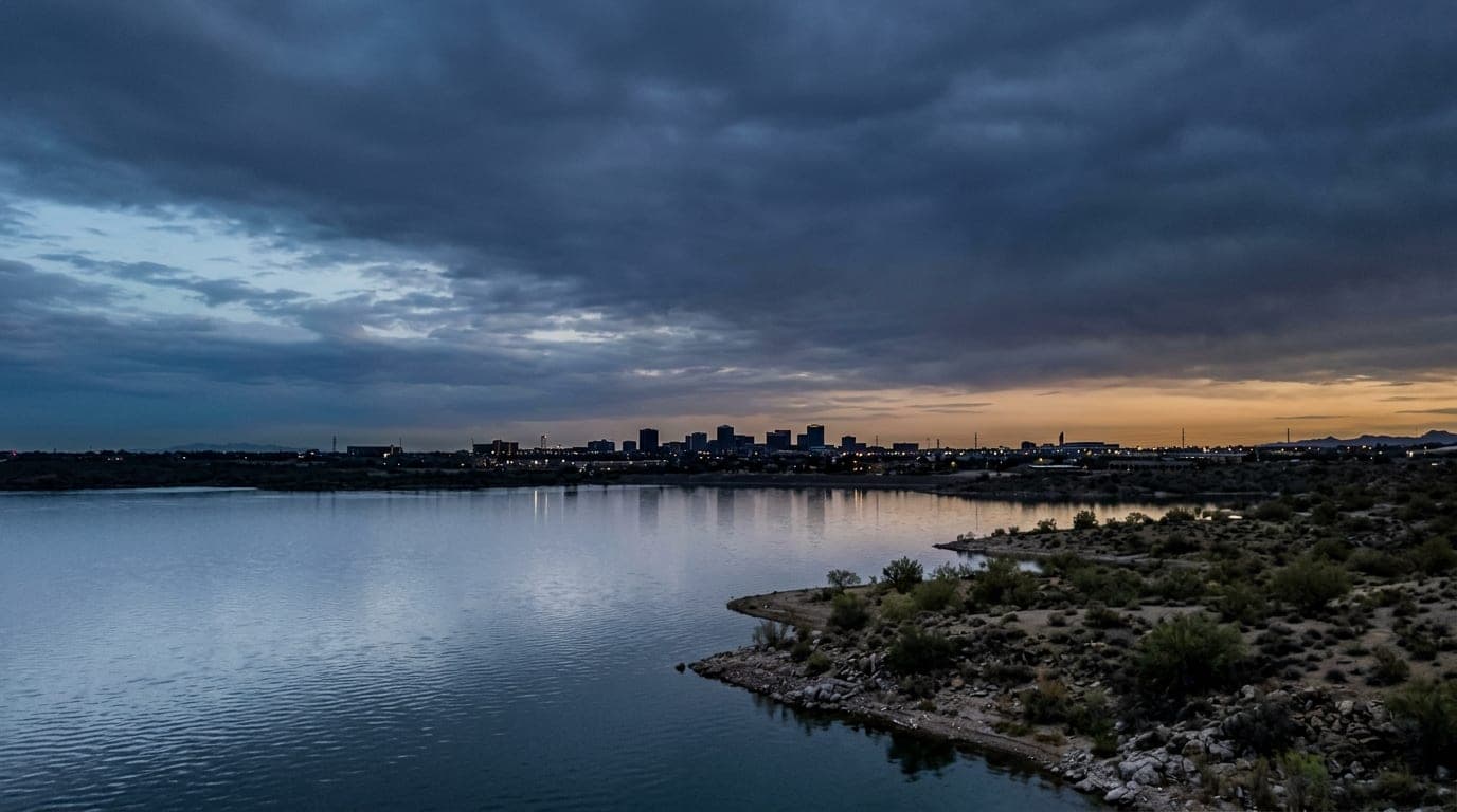 An overhead 50mm flat-lay view of the shimmering Lake Pleasant shoreline at dawn. The quiet, cool-toned water occupies the...