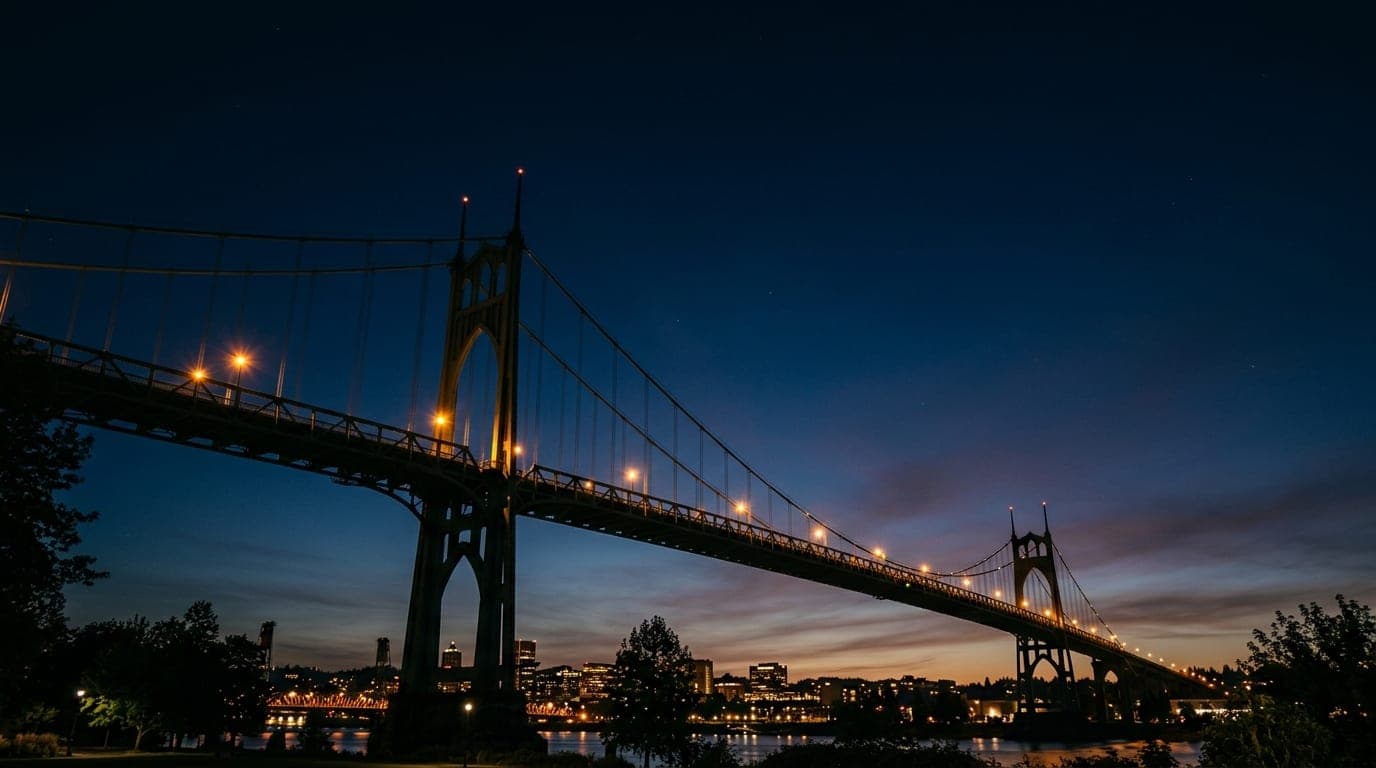 A low-angle shot of the iconic St. Johns Bridge at midnight. The steel arches tower above, silhouetted against the dark sk...