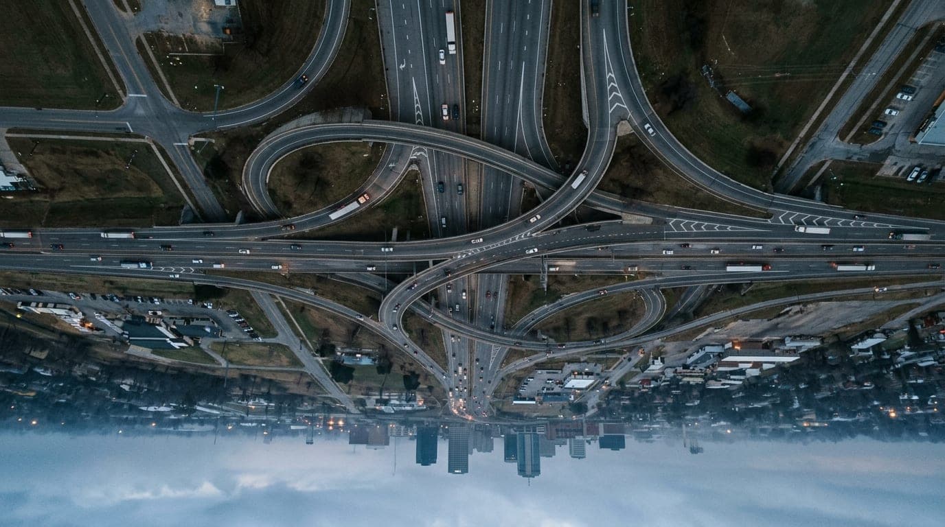 Overhead 50mm flat-lay of the gray asphalt geometry at the Kellogg and I-135 interchange during an overcast morning, with...