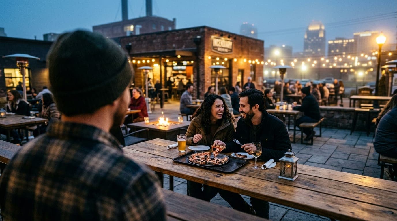 Over-the-shoulder, tilt-shift view at blue hour in the Incendiary Brewing courtyard. A couple sits at a communal wooden ta...